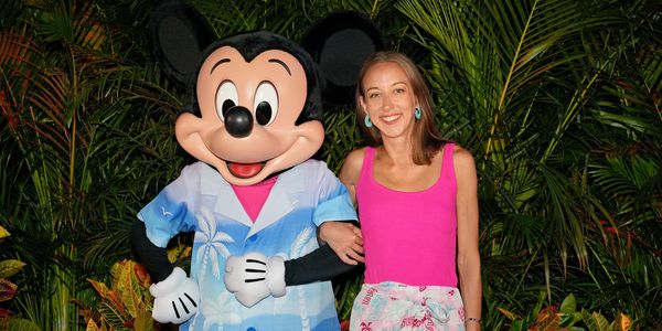 A woman poses happily with Mickey Mouse in tropical attire surrounded by lush greenery.