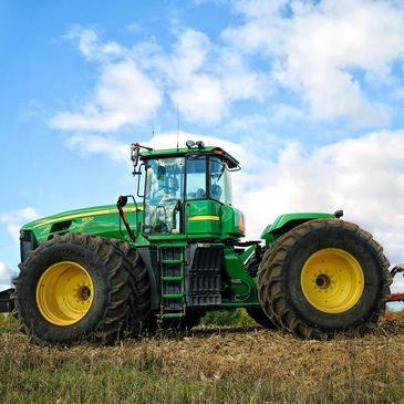 A large green tractor with oversized tires under a blue sky.