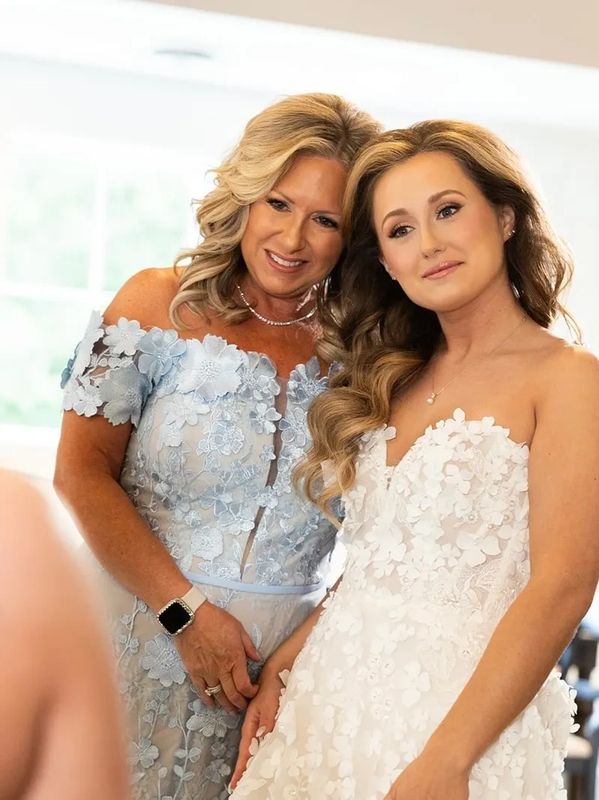 A bride and her mother share a tender moment, both in elegant floral dresses.