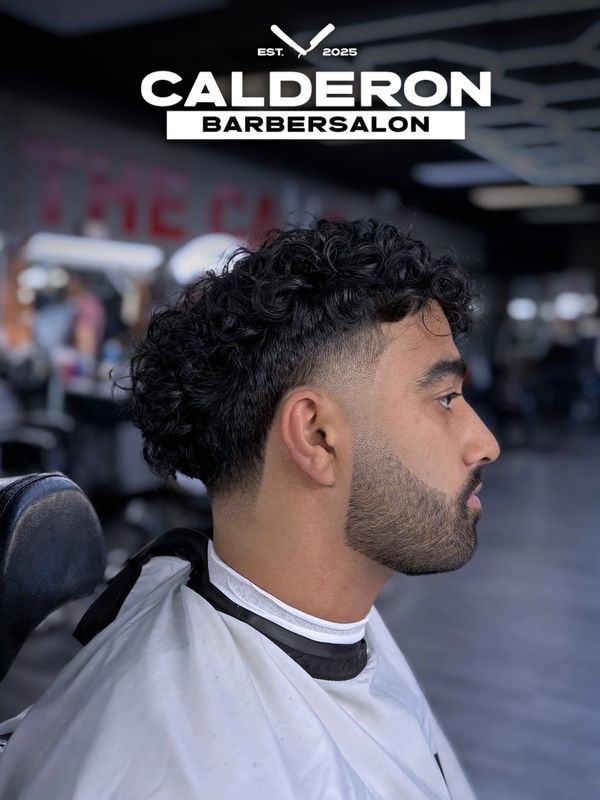 Side profile of a man with a fresh curly fade haircut and beard at Calderon Barbersalon.
