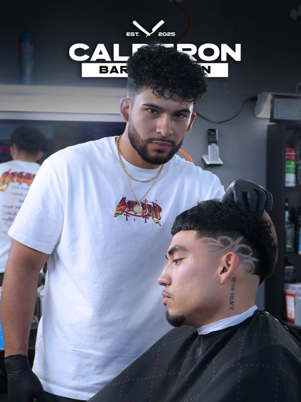 Barber styling a client's haircut with intricate shaved designs on the side.