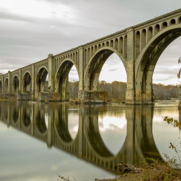 A long arched bridge reflected in calm river water under a cloudy sky.
