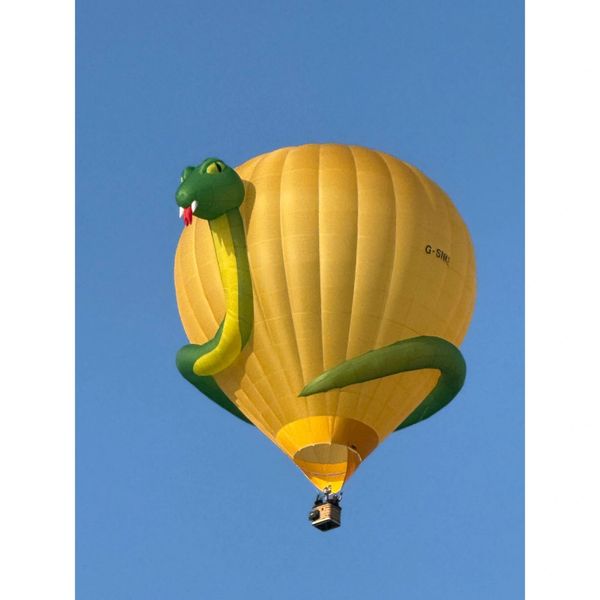 Yellow hot air balloon shaped like a snake against a clear blue sky.