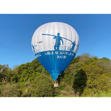 A blue and white hot air balloon flying over green trees under a clear sky.