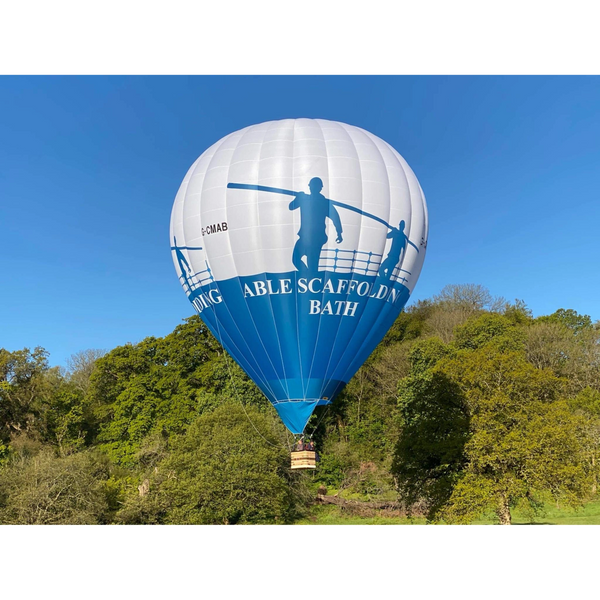 A blue and white hot air balloon flying over green trees under a clear sky.