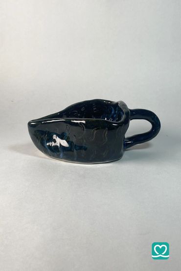 Glossy black ceramic sauce bowl with a handle on a plain background.