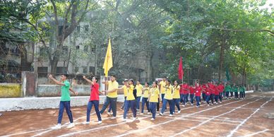 Students in colorful uniforms marching on a track during a school sports event.