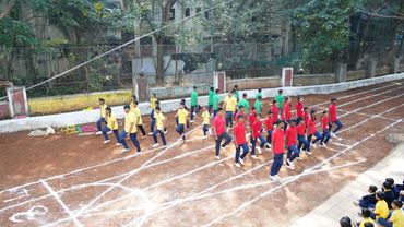 Students in colorful uniforms practicing marching on a sports ground.