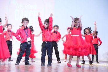 Children in red outfits performing a dance on stage.