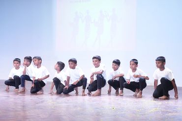 Young boys in white shirts and black pants squatting on stage during a performance.