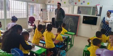 Young students in yellow uniforms are drawing in a classroom with attentive teachers.