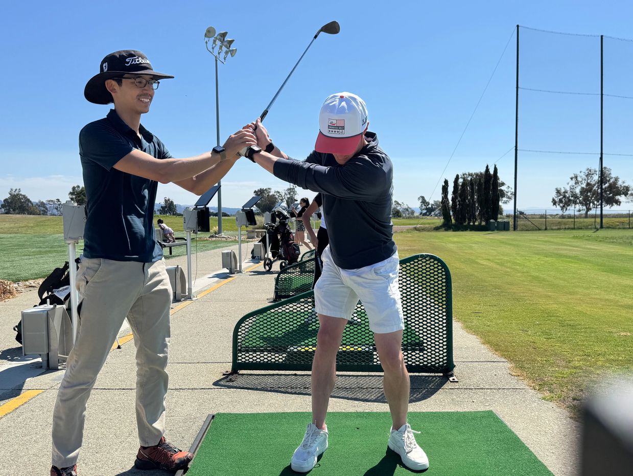 Golf instructor helps a player with swing technique at a driving range.