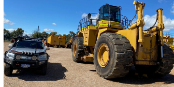 Large yellow construction vehicle next to a silver SUV.