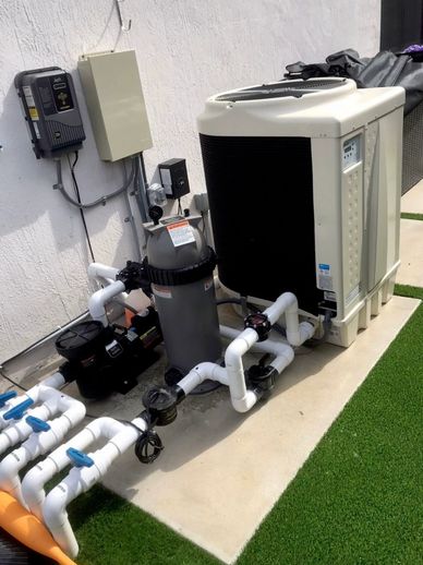 Pool equipment setup with pump, filter, heat pump, wall-mounted controls and PVC plumbing.