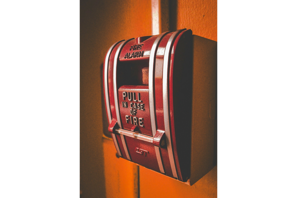 Close-up of a red fire alarm pull station on an orange wall.