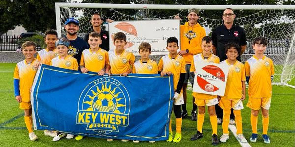 Youth soccer team from Key West posing on field with a banner and oversized check.