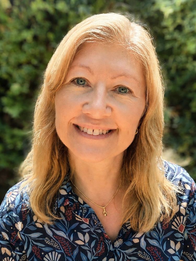 Headshot of Leah Clements smiling and sitting in a garden in the sunshine.