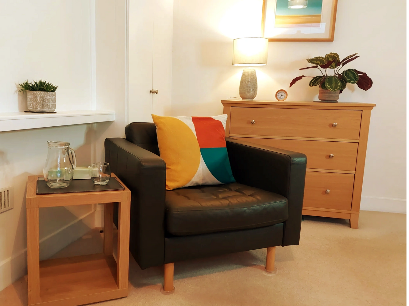Brown leather armchair, side table, chest of drawers with lamp and plant on top in therapy room.