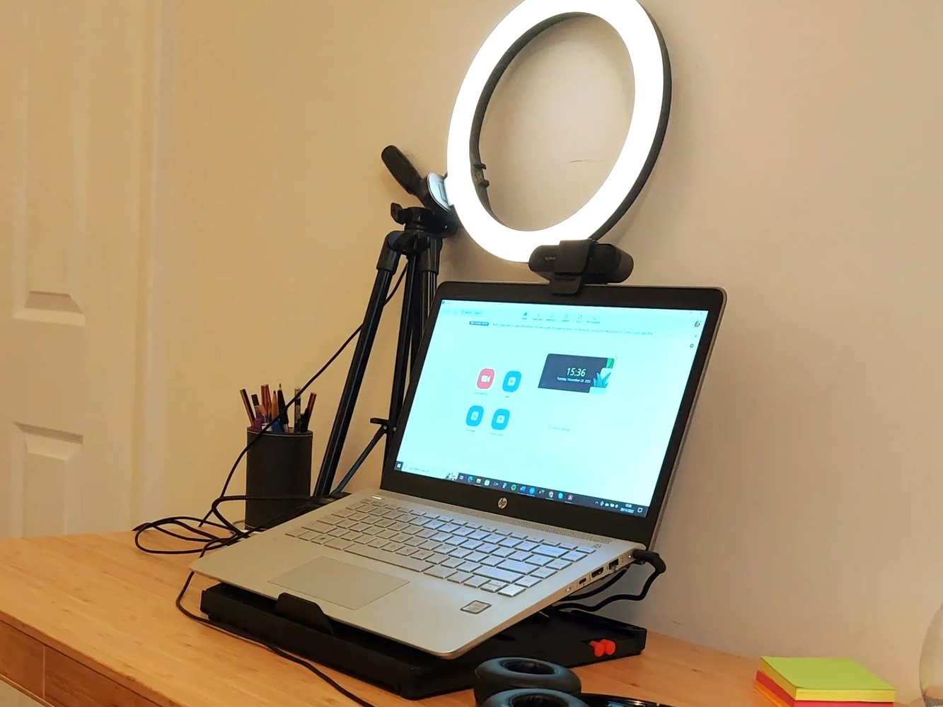 Laptop, ringlight, pen holder and headphones on a desk.