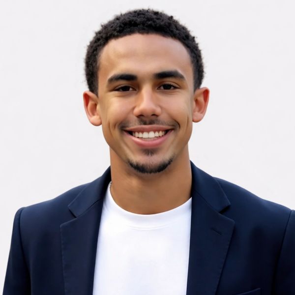 Smiling young man in a navy blazer and white shirt against a plain background.