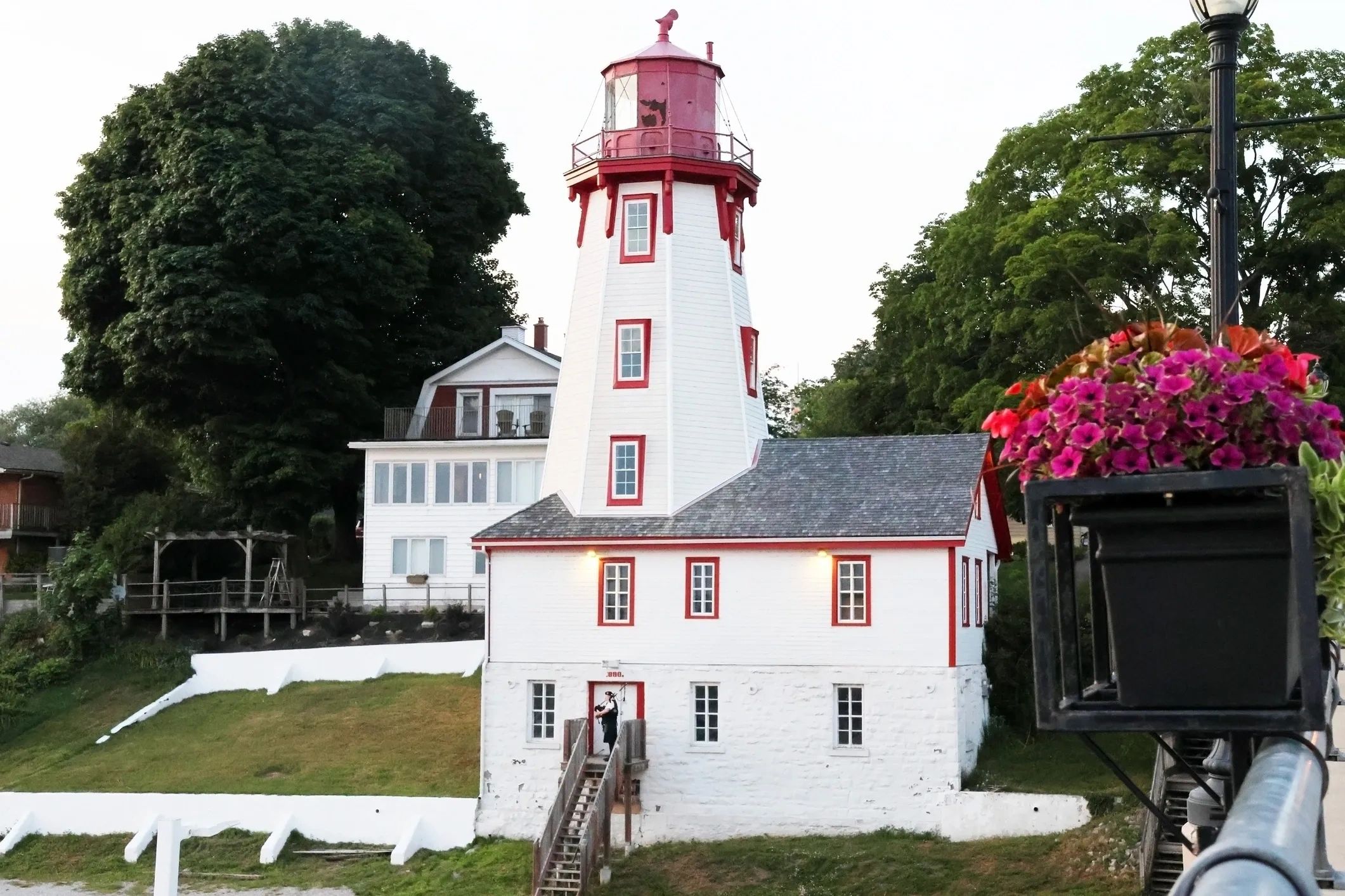 White building with red lighthouse tower surrounded by trees and flowers.