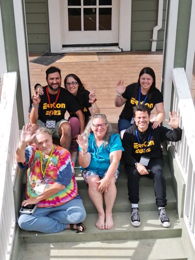 Group of six people waving and smiling on front steps.