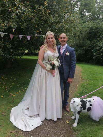 Bride and groom posing with their dog at an outdoor wedding. Wedding Dog Chaperone 