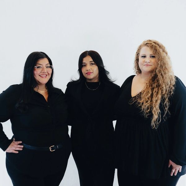 Three women dressed in black posing against a white background.