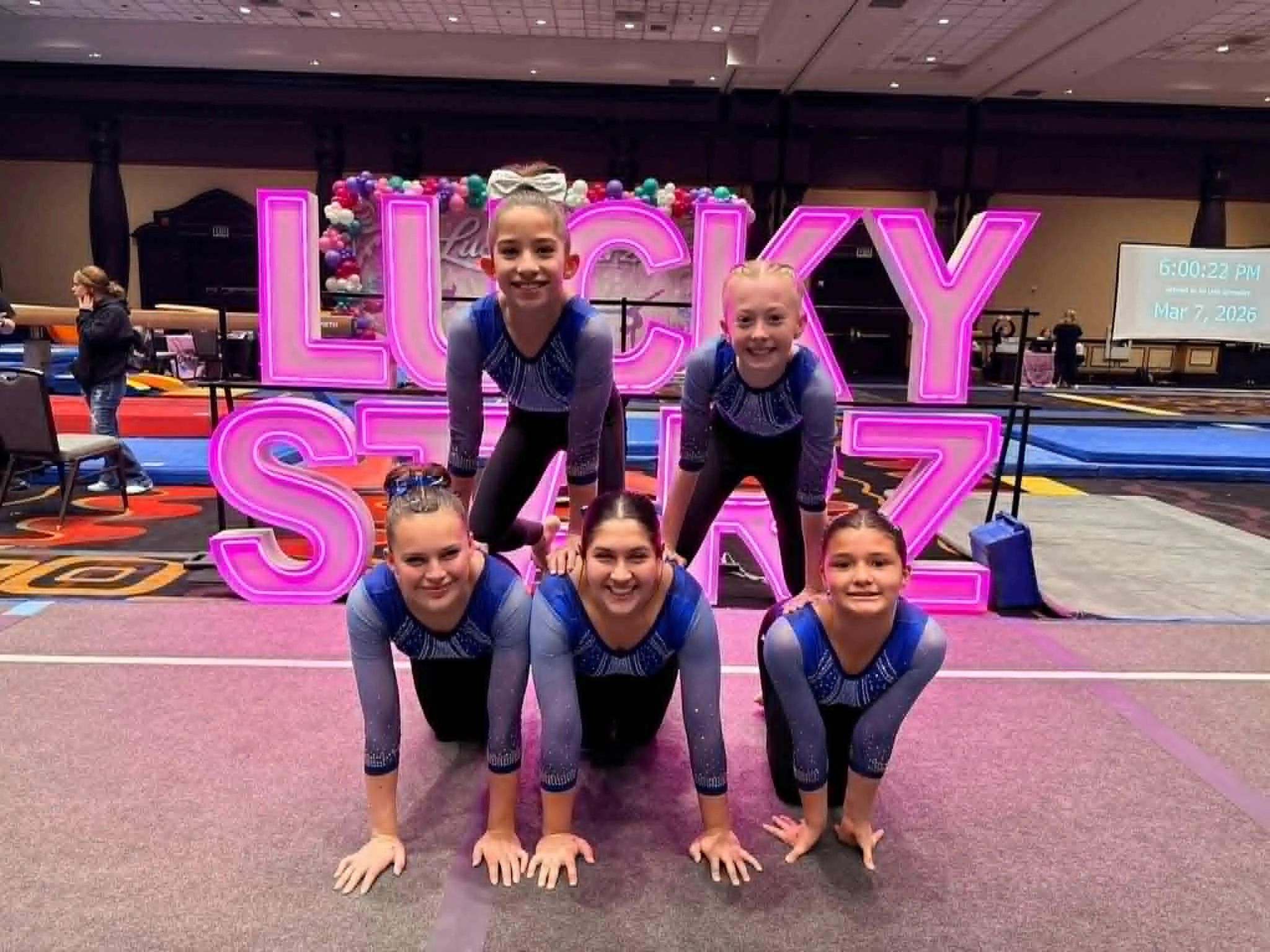 Gymnastics team posing in front of a neon Lucky Stars sign.