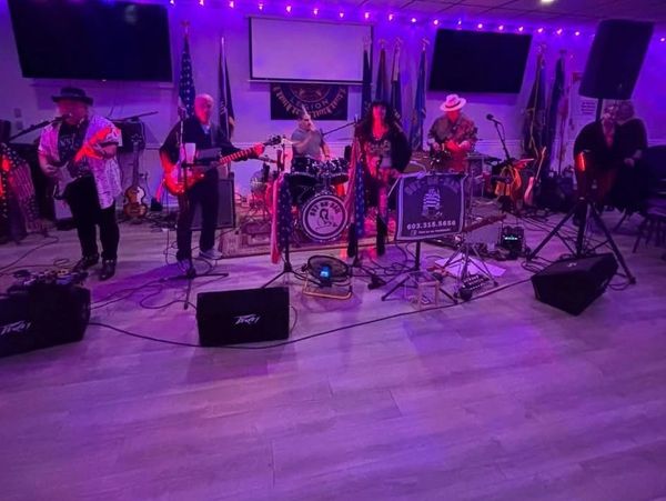 A band performs on stage with purple lighting in a small venue.