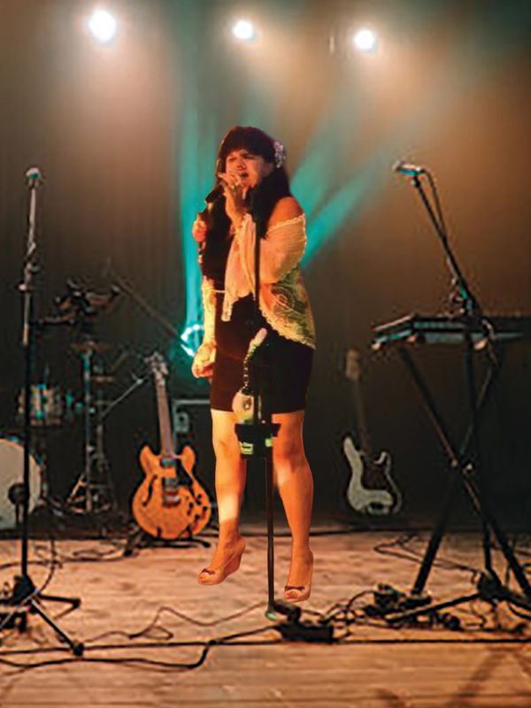 A woman passionately singing on stage with musical instruments in the background.