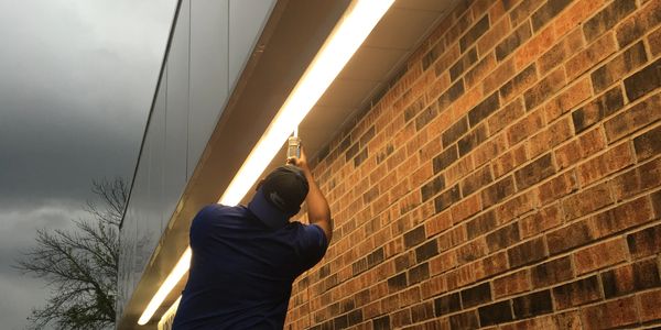 A man installs or repairs a light fixture on a brick building exterior.