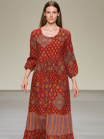 Model walks runway in a long, patterned red dress with balloon sleeves.