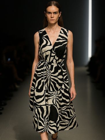 Model walking runway in a black and white abstract patterned dress with ankle-strap heels.