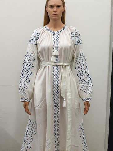 Woman in a white dress with blue geometric embroidery and a waist tie.