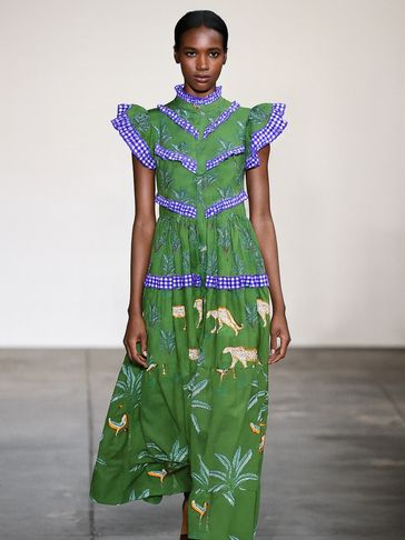Model wearing a green dress with blue ruffles and animal prints walking on a runway.