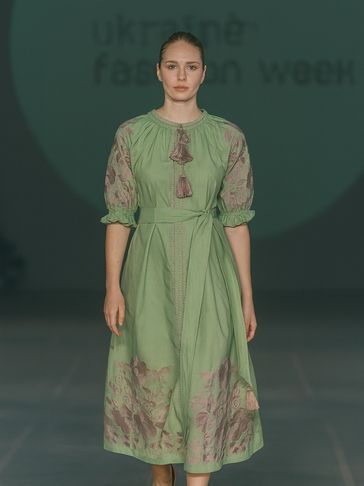 Model walking runway in a green embroidered dress with tassels at Ukrainian Fashion Week.