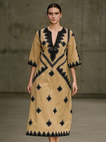 Model wearing a tan dress with black geometric patterns walking on runway.