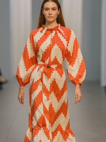 Model wearing a bold orange and white zigzag patterned dress with puffed sleeves.