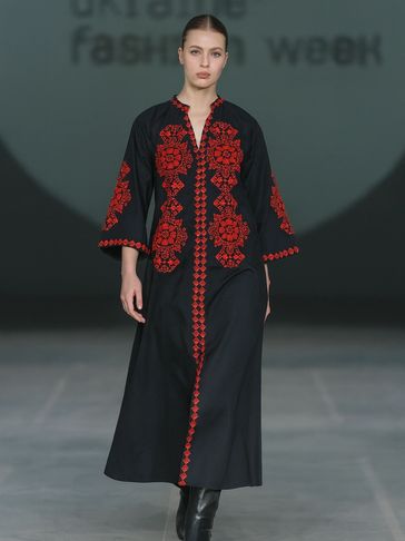Model walks runway in black dress with red floral embroidery at Ukraine Fashion Week.