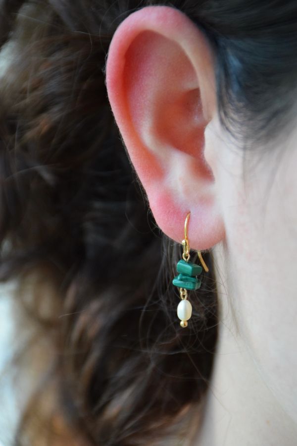 Close-up of an ear wearing a green and pearl dangling earring.