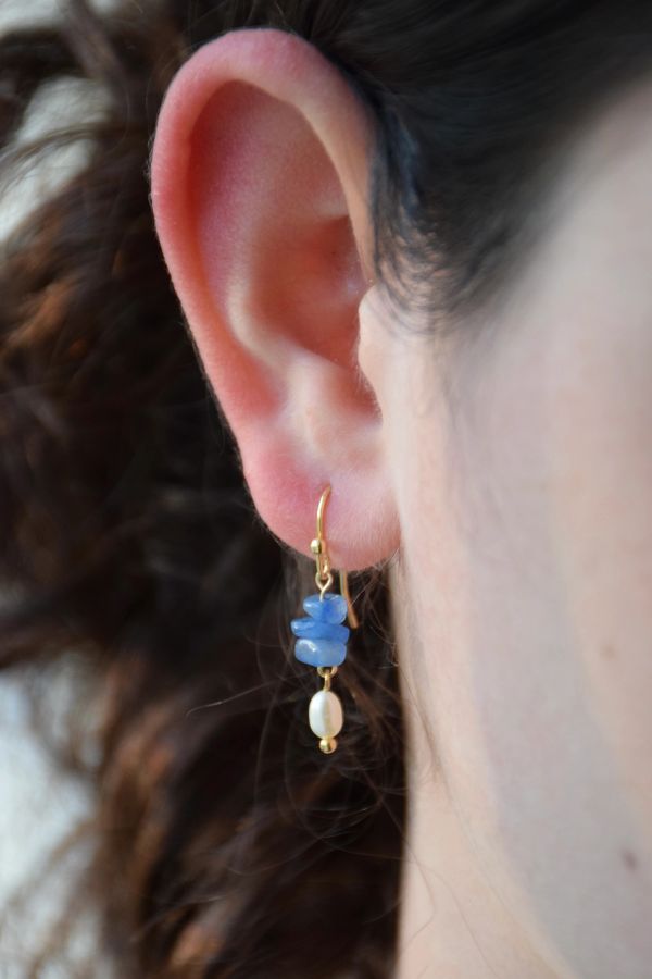 Close-up of ear with gold earring adorned with blue stones and a small pearl.