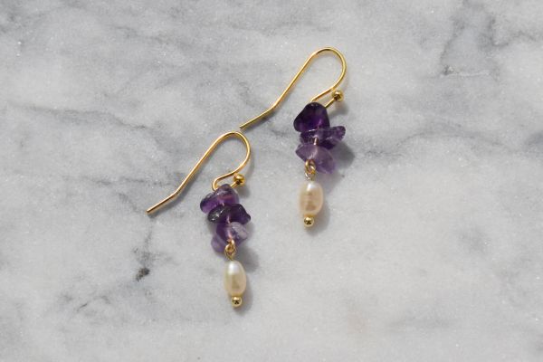 Elegant gold earrings with amethyst stones and pearl drops on marble.