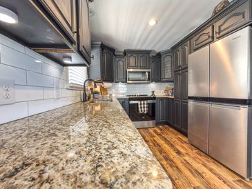 Modern kitchen with granite countertop, dark cabinets, and stainless steel appliances.