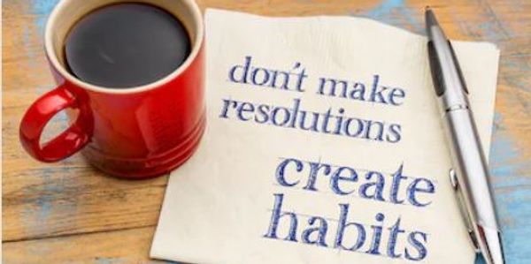 a  red mug of black coffee on a napkin that reads: Don't make resolutions create habits