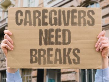Person holding a cardboard sign that says 'Caregivers Need Breaks'.