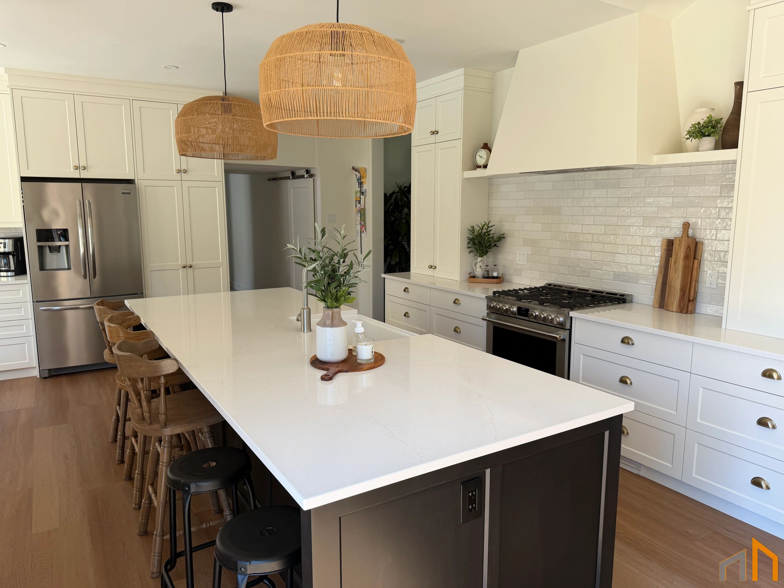 Modern kitchen with white island, wooden stools, and woven pendant lights.