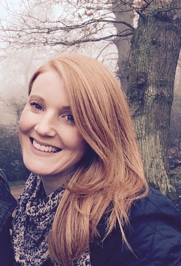Smiling woman with red hair outdoors near a tree in foggy weather.
