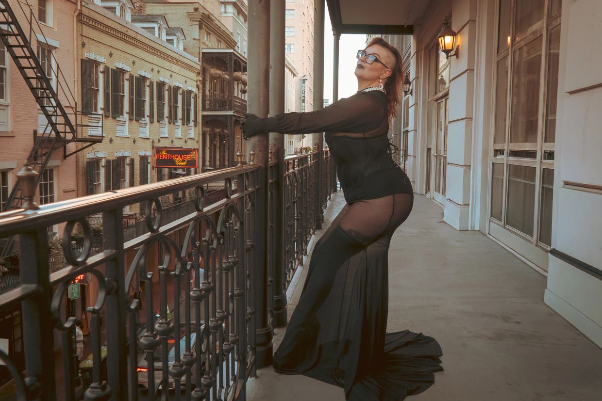 Person in black outfit posing on a balcony in a city.