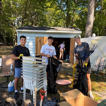 Three boys cleaning up outdoors with tools and trash bags.